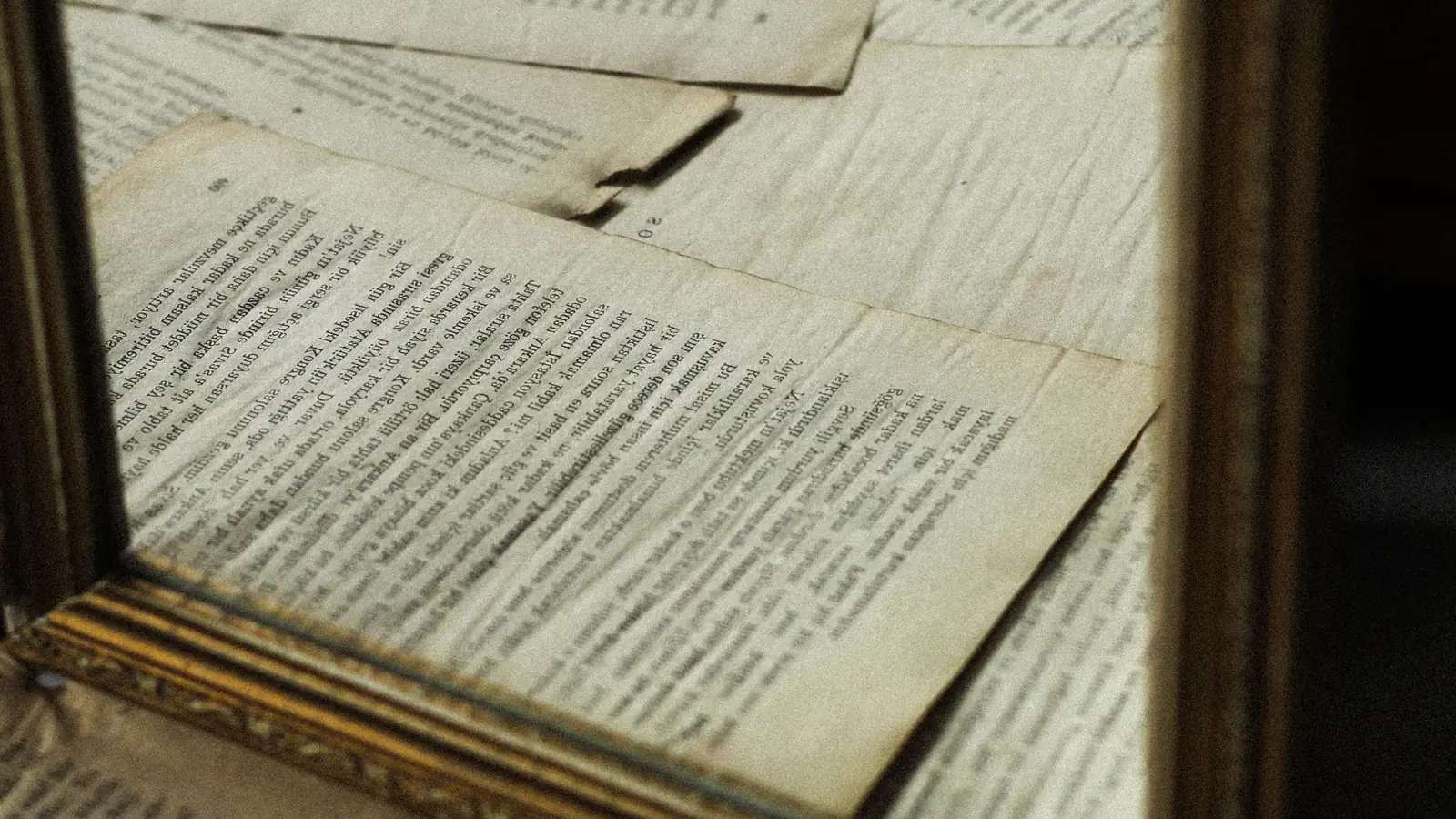 Yellowed book pages reflected in a gold-framed mirror